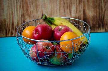 Metal fruit bowl on a wooden surface. Close. Bananas, oranges apples