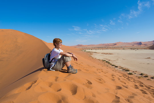 Relaxed tourist sitting on sand dunes and looking at the stunning view in Sossusvlei, Namib desert, best travel destination in Namibia, Africa. Concept of adventure and traveling people