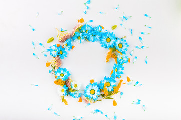 The wreath of blue and orange flowers and blue petals on a light background. Top view. Flat lay.