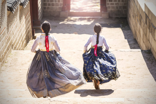 Two Korean Girls dressed in traditional dress running down stairs in Seoul street