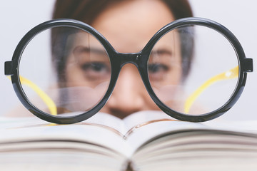 Nerdy young asian woman student with old big round glasses bored with reading book