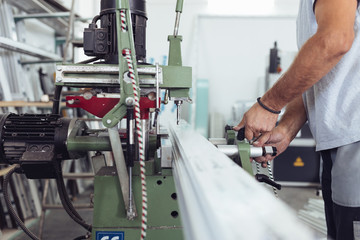 Manual worker doing his job on big machine for profile cutting. Manufacturing jobs. Selective focus. Factory for aluminum and PVC windows and doors production.