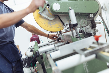 Manual worker doing his job on big machine for profile cutting. Manufacturing jobs. Selective focus. Factory for aluminum and PVC windows and doors production.