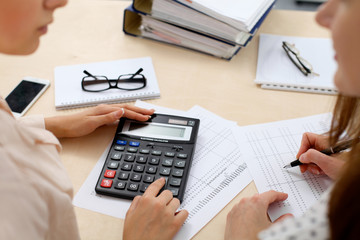 Fototapeta na wymiar Two female accountants counting on calculator income for tax form completion hands closeup. Internal Revenue Service inspector checking financial document. Planning budget, audit concept