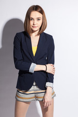 stylish young smiling woman in dark blue blazer and bright mini-shorts on white background