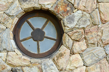A Round metal window on the stone wall of an unidentified residence 