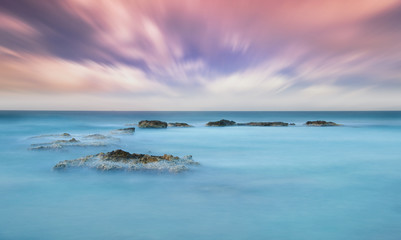Obraz premium Stones in the sea on a long exposure during sunset.