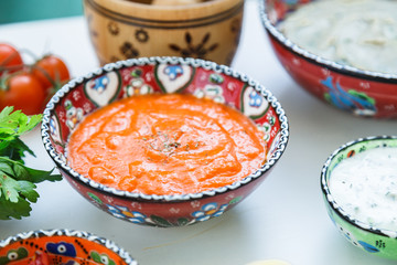 Small bowls of homemade harissa and tzatziki with meze on a table.
