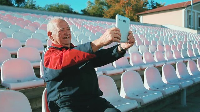 Smiling elderly man with phone. Senior male on a bench. I miss my relatives. Grandpa calls home. Elderly man and gadgets. Grandpa makes selfie.