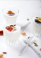 Yogurt in glass cups with nuts,pistachios and fresh figs.Breakfast,Dessert, Pudding on a white background.Food or Healthy diet concept.selective focus.Top view.