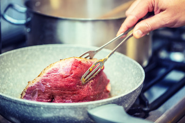Beef steak. Chef in a restaurant kitchen use ceramic pan for preparation of beef steak.