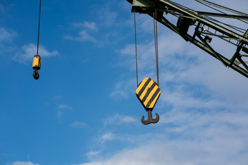 Black and yellow cranes hooks hanging on steel ropes