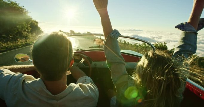 Happy couple driving on country road into the sunset in classic vintage sports car