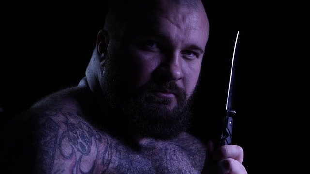 Bald tattoed bearded muscular gangster with a knife. 4K UHD