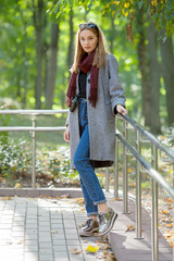 Beautiful stylish young woman in a warm scarf blue jeans trendy shoes and cozy coat walking along in fall city park