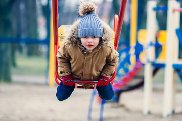 Cute little boy riding on swing in park and looking at camera