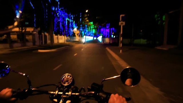 Camera on Motorcycle Moves along Dark Street by Lit Sideroads