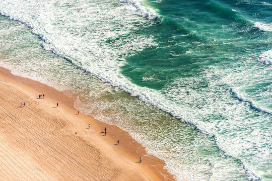 Aerial view from above of ocean, sea beach and water waves with people on sand shore with emphasis of the scale of people and nature. Surfers Paradise, Gold Coast, Queensland Australia