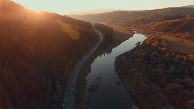Aerial: Beautiful sunset in the highlands. Forest, country road and the river bed at sunset. Twisty riverbed. The road parallel to the river. Amazing places in the world. Beautiful nature in Siberia
