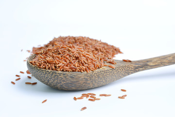 Uncooked red rice in a wooden spoon, white background 