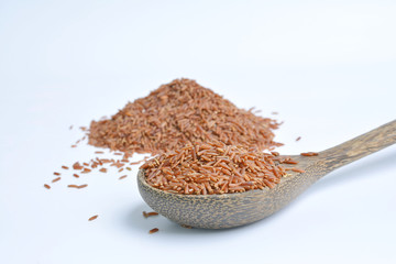 Uncooked red rice in a wooden spoon, white background 