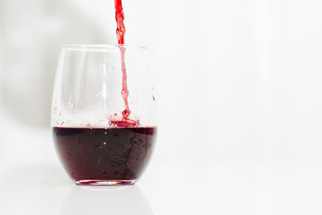 Red wine is pouring into a glass. An aperitif in the goblet is on the white background. 