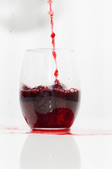 Red wine is pouring into a glass. An aperitif in the goblet is on the white background. 