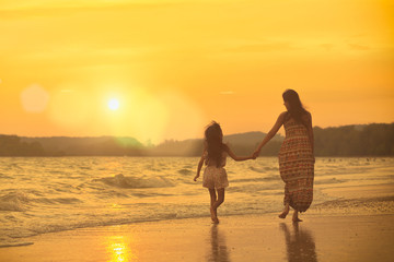 Fototapeta premium Mother and daughter walking on the beach with sunset