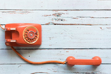 Retro orange-red telephone on the old wooden table with copy space for text or your subject in the...