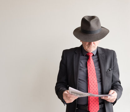 Older man dressed for a day at the horse races in black suit, red tie and hat, reading newspaper racing guide