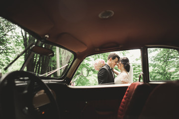 Beautiful wedding couple posing near splendid retro car