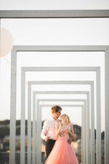 Pretty sunny outdoor portrait of young stylish couple while kissing on the roof with city view