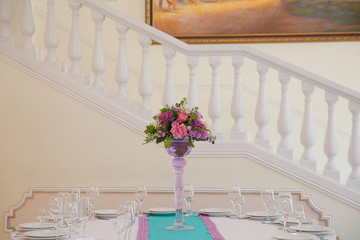 Bouquet in high vase stands in the middle of a dinner table on b