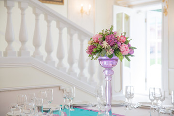 Pink and violet bouquet stands in a high vase on round dinner ta