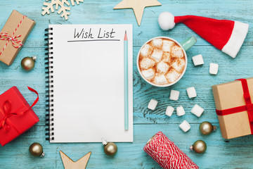 Cup of hot cocoa or chocolate with marshmallow, holiday decorations and notebook with wish list on...