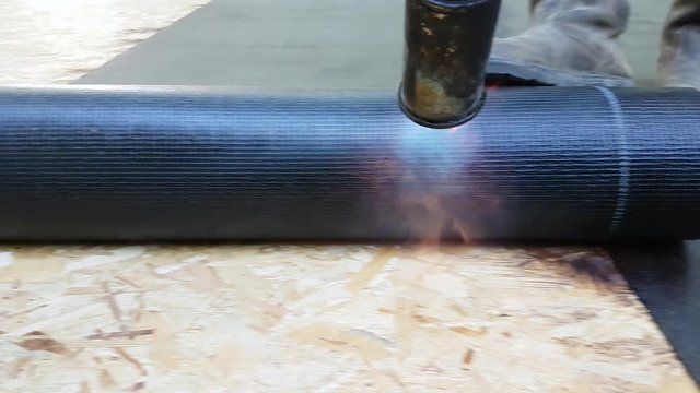 Detail of asphalt roll roofing installation. Fire from bitumen torch.