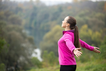 Portrait of an attractive woman outdoors in a sporstwear, her hands outstretched. Concept photo, side view