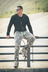 young fit man with inline skates rest in summer park after workout outdoor rollerskater