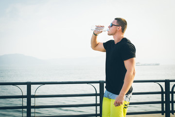 young fit man with inline skates drink water after workout outdoor rollerskater on promenade