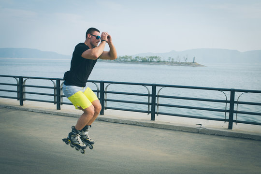 Fit man rollerskater jump inline rollers perform trick on the promenade