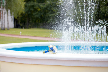 Blue and white wedding bouquet lies behind a fountain