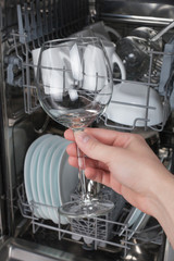 Hand holding clean glass on a background of the dishwasher
