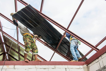Naklejka premium Roofing construction workers install metal sheet on the roof.