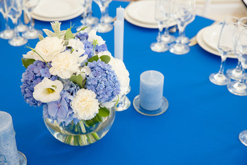 Blue candles surround a tender bouqet of hydrangeas on a dinner