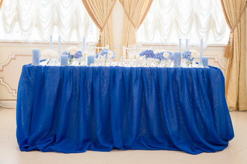 Newlyweds table stands covered with blue cloth and decorated wit