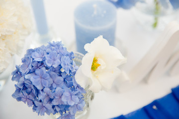 White and blue flowers stand in a small vase behind candles