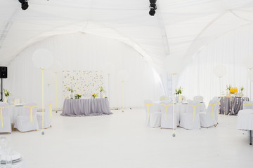 Round tables covered with white and gray cloth stand in a pavili