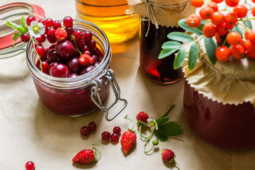 Fruit preserves and raw strawberries , cherries , rowans berries on a kitchen table, organic meal and dessert concept