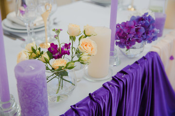 Bouquets of roses and lilacs stand on the table between candles