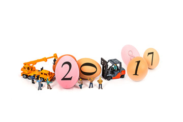 miniature worker team building standing front of forklift and truck with egg and 2017 number , on white background.abstract background to Happy new year decoration 2017 concept.